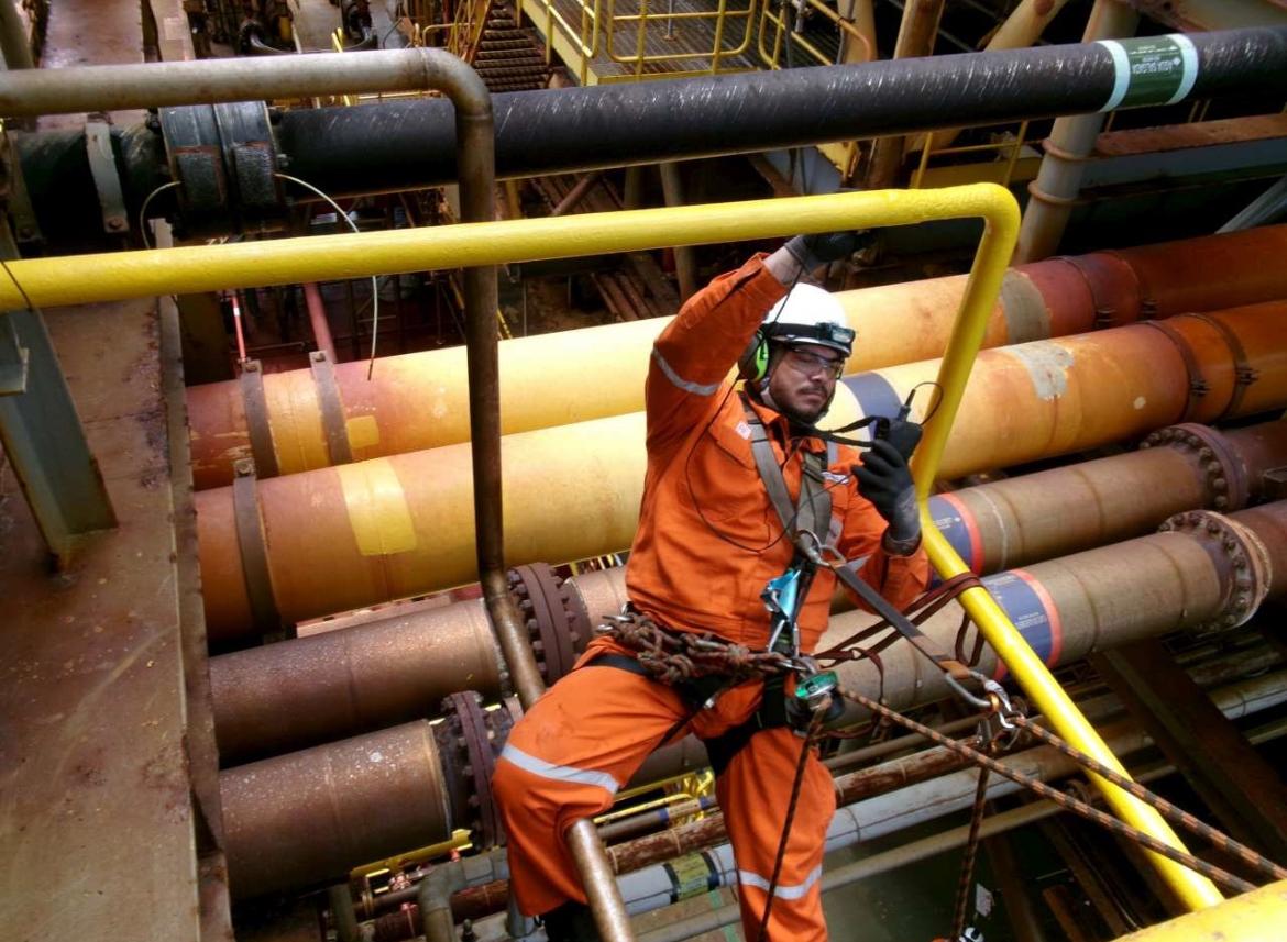 Técnico em acesso por cordas inspecionando linhas de processo em plataforma