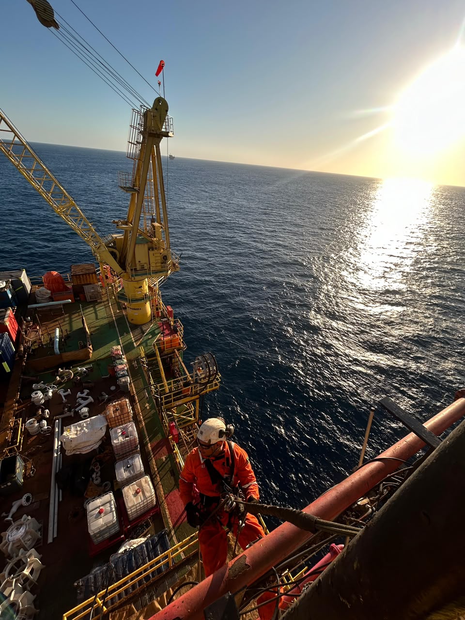 Técnico em acesso por cordas em plataforma offshore ao pôr do sol