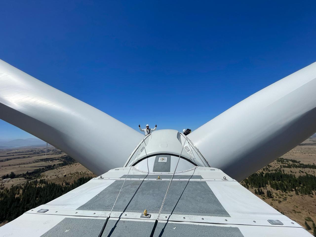 Topo de aerogerador com pás em primeiro plano e equipe ao centro